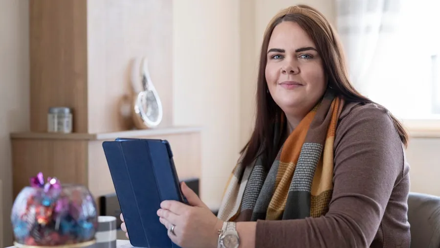 Foto von Sarah, die an einem Tisch sitzt. Vier Jahre nach Sarahs erster Diagnose stellte sie einen Zusammenhang zwischen ihren Blasenproblemen und ihrer MS her. 