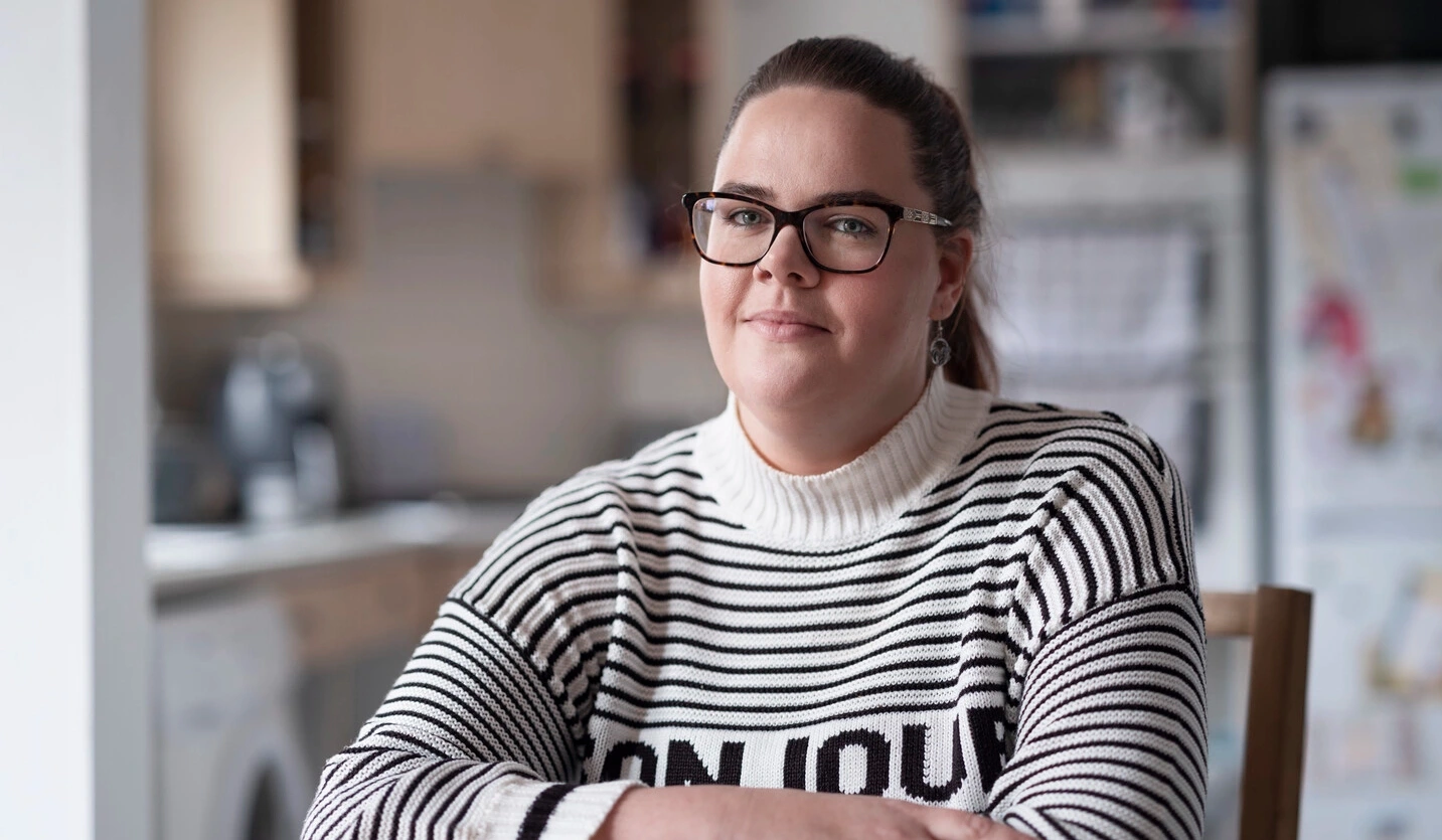 Sarah, eine Nutzerin von intermittierenden Kathetern, die mit MS lebt, sitzt an einem Tisch. 